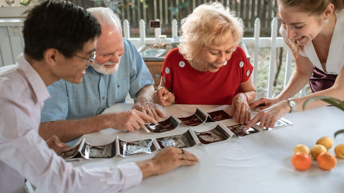 An elderly couple with family happily viewing ultrasound pictures at a table indoors.