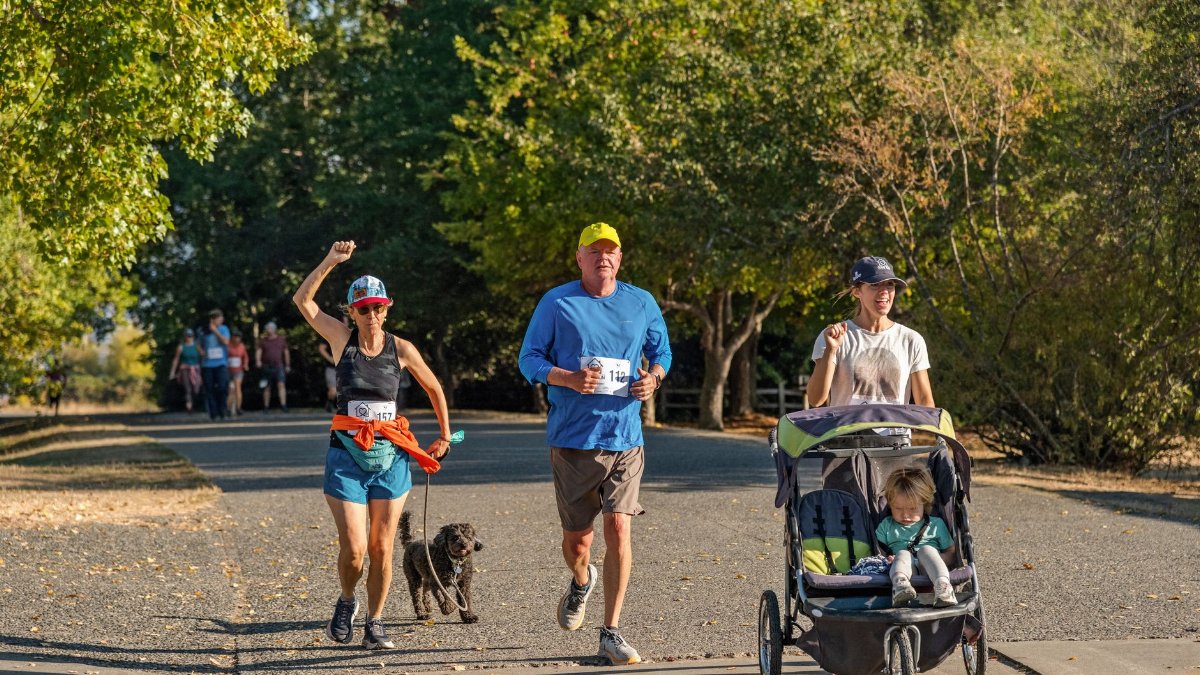 Participants in a family fun run at a local park, featuring adults, children, and pets.