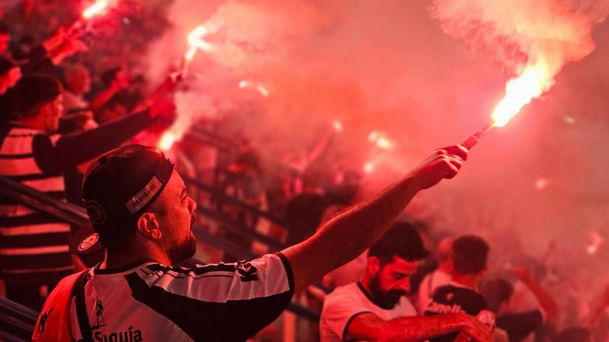 Energetic crowd celebrating with red flares at a sports event, creating a vibrant and passionate atmosphere.