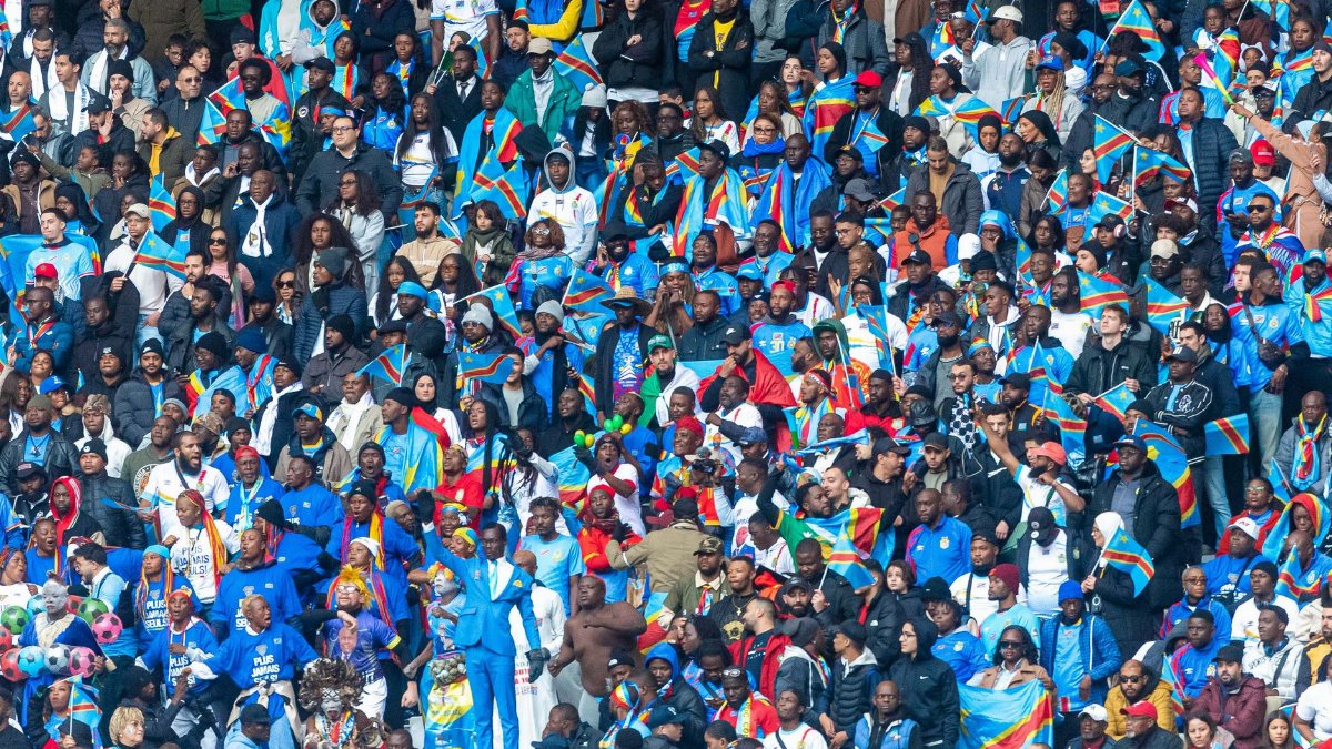 Packed stadium with diverse crowd waving Congolese flags, celebrating unity.