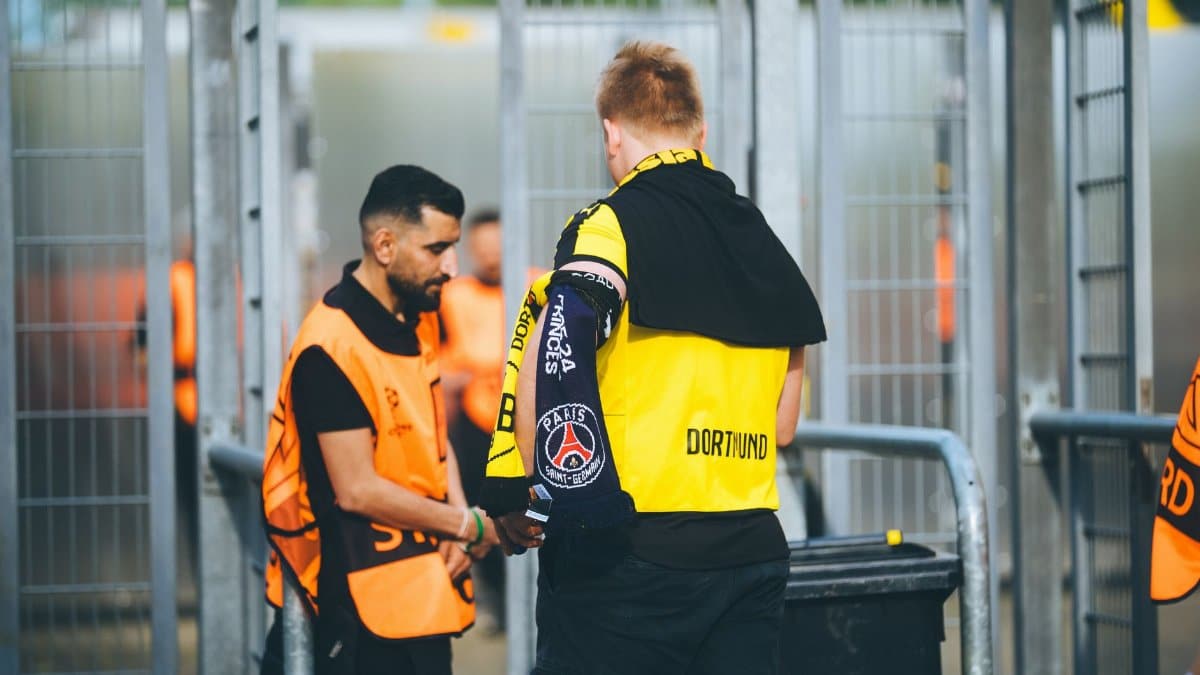 Security personnel and a fan at a football stadium checkpoint in Dortmund, Germany.