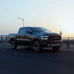 A sleek black Ram pickup truck speeds down an empty highway at sunrise, showcasing modern design and power.