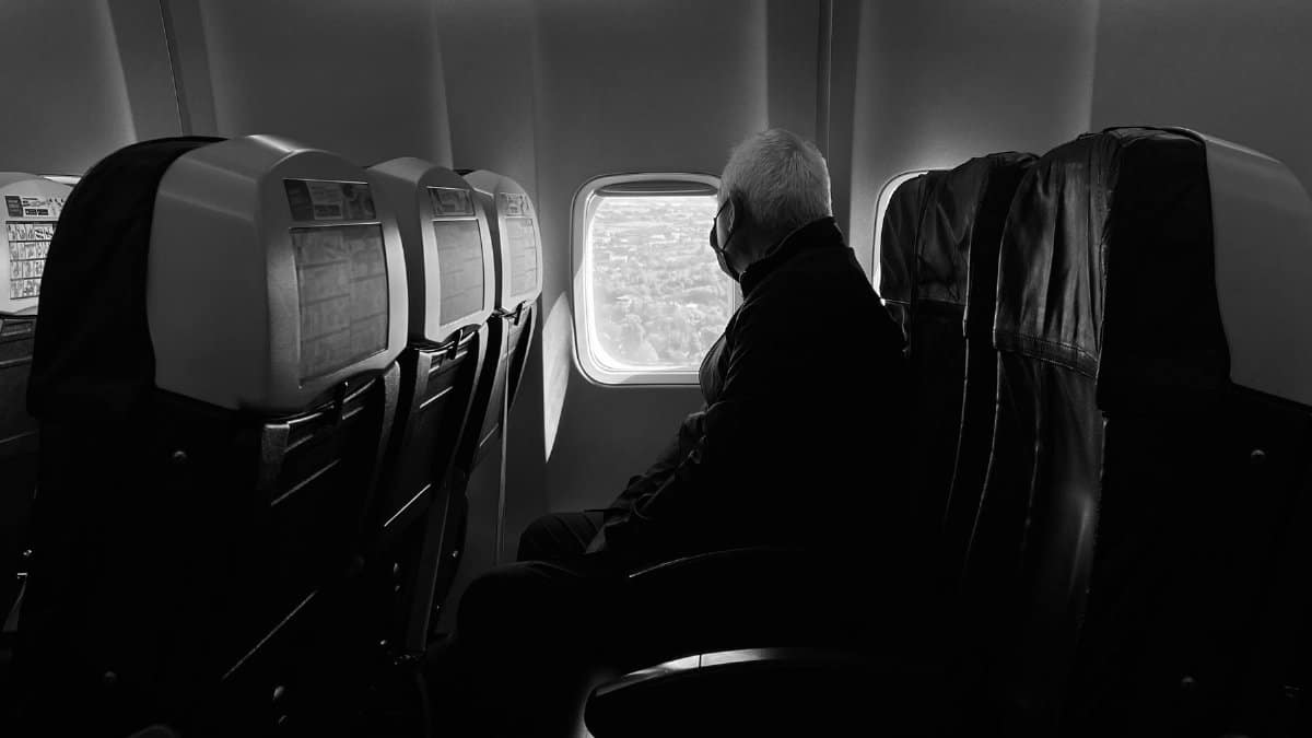 A man wearing a mask gazes out an airplane window during a daytime flight.
