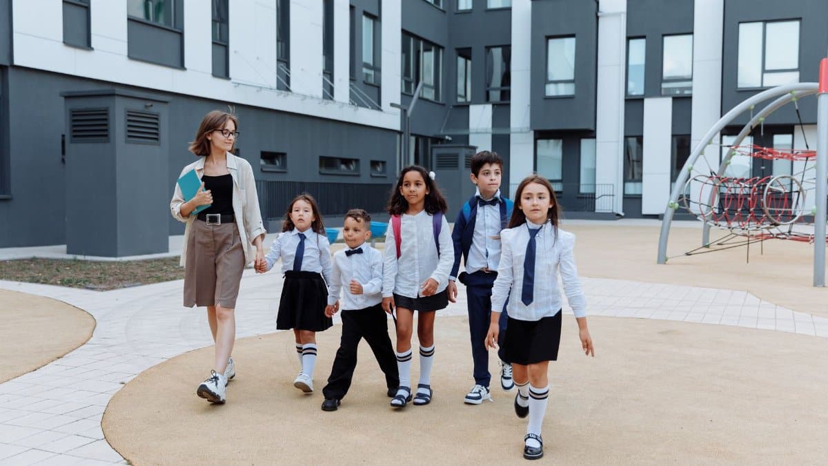 A teacher leading a group of diverse students on a modern school campus walkway.