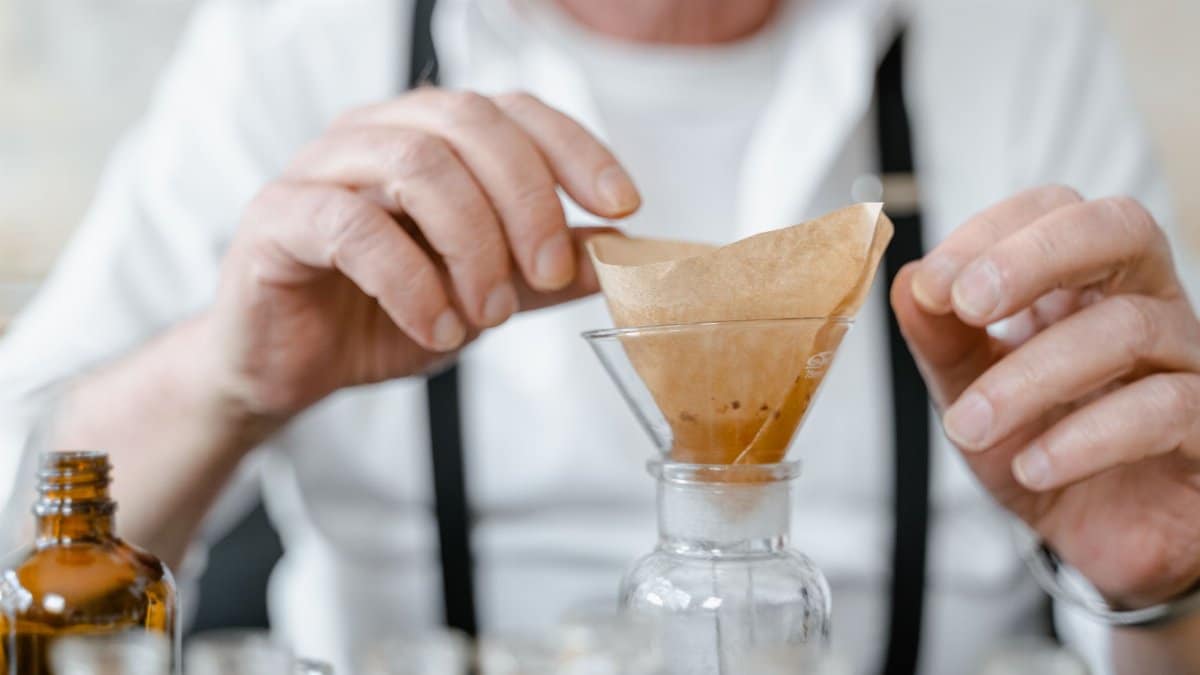 Close-up of an elderly scientist using paper filters in a chemistry experiment with glass apparatus.