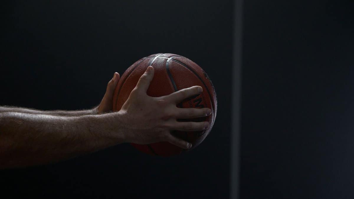 Dramatic close-up of a basketball player's hands holding a ball against a dark background.