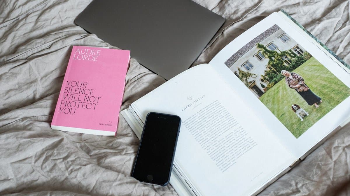 Top view of arranged art book with smartphone and laptop placed on soft blanket on comfortable bed in modern light room