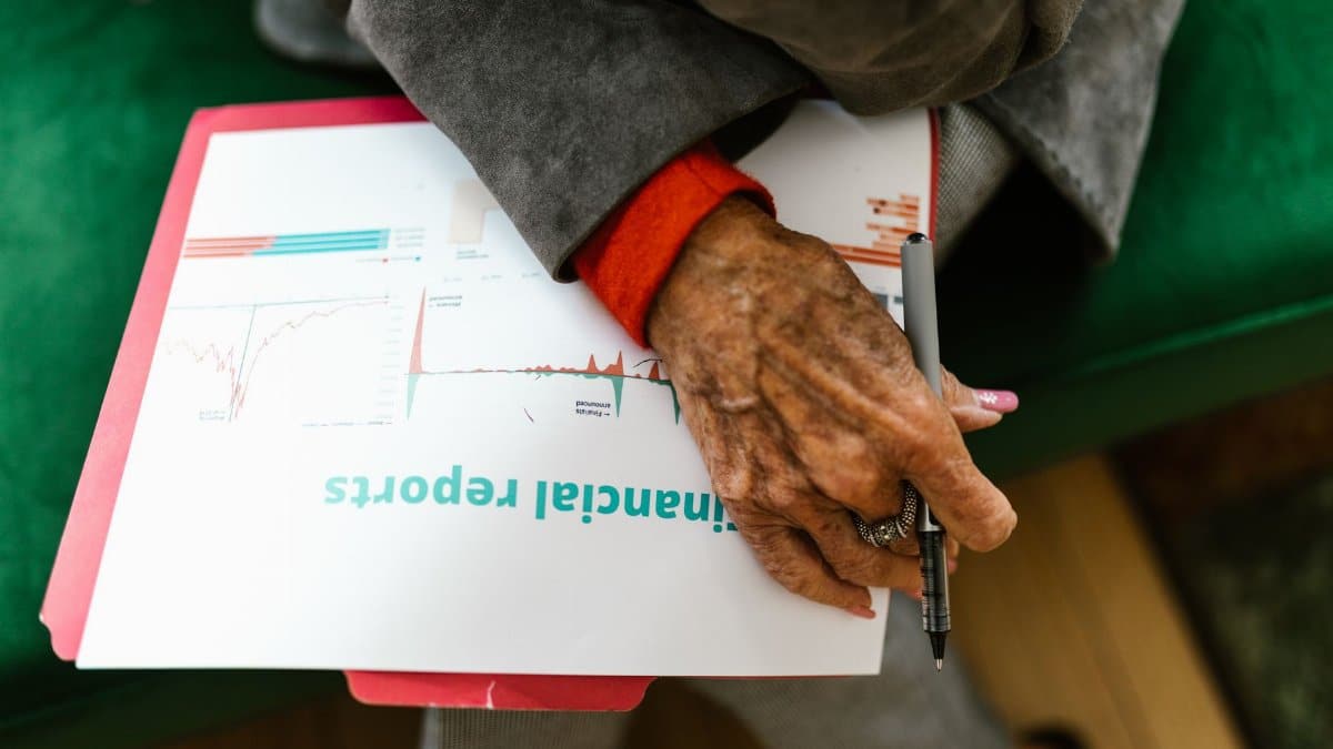 Close-up of an elderly woman holding a pen with a financial report.