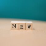 Wooden blocks spelling out 'NEW' on a wooden surface against a teal background.