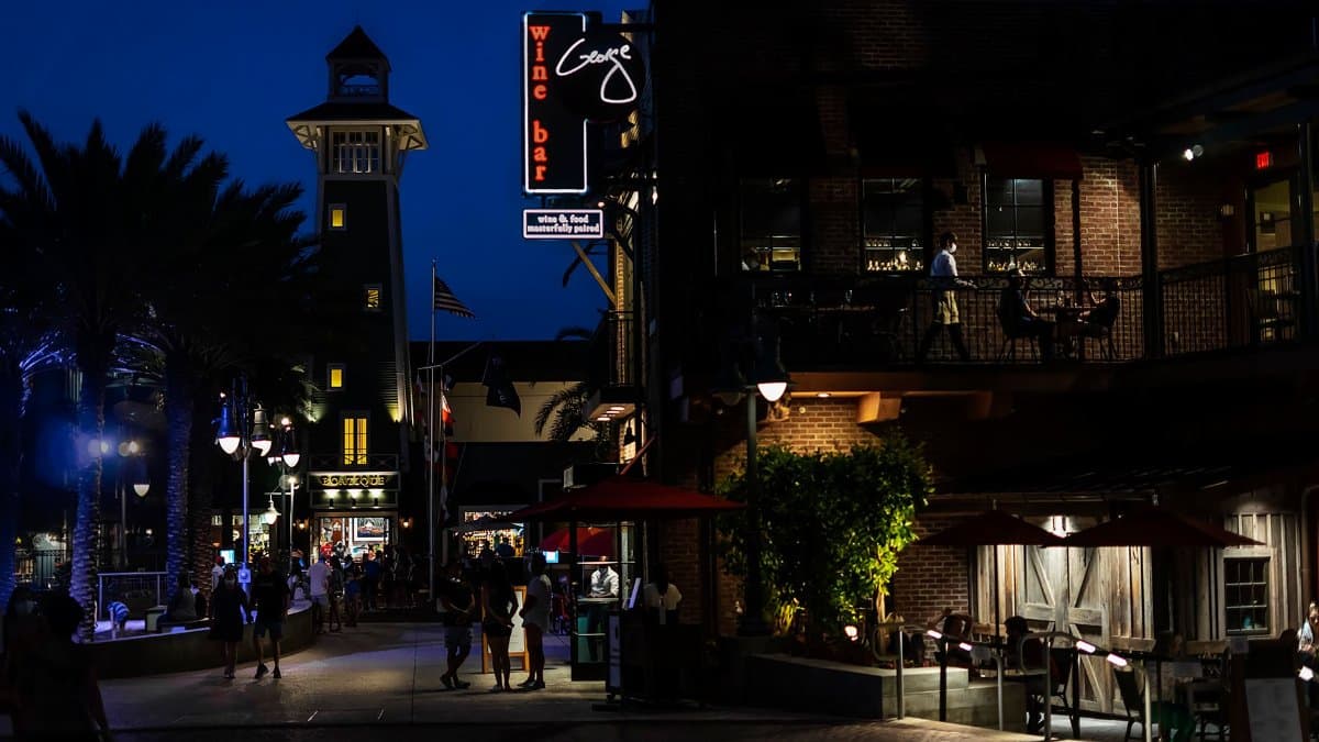 Nighttime view of a lively street in Orlando featuring a tower and bustling wine bar.