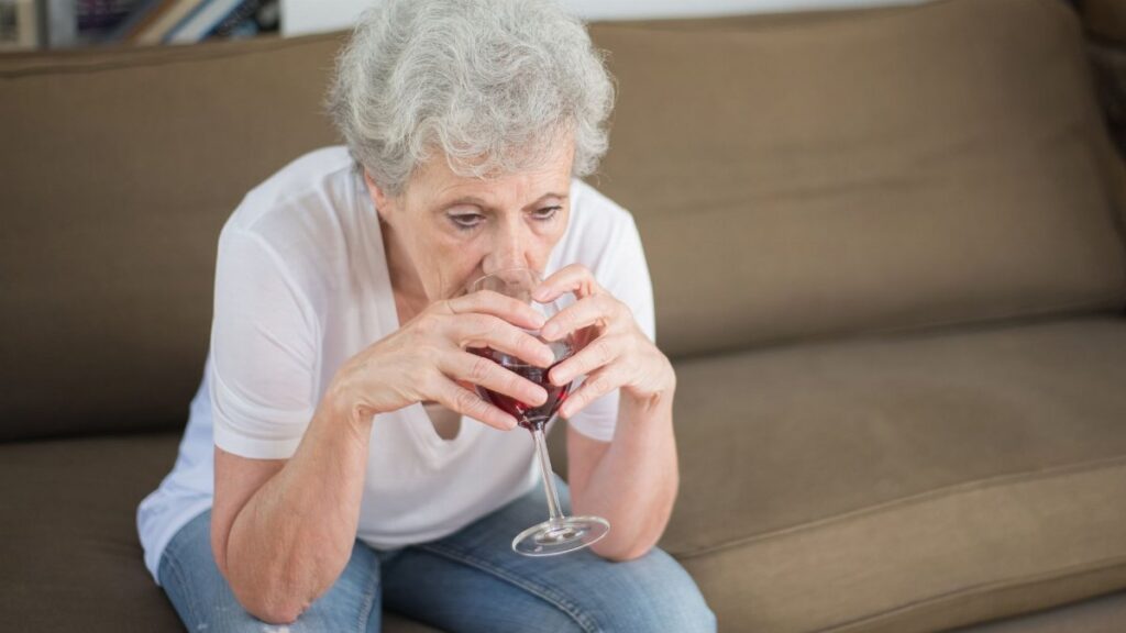 Senior woman in contemplation, drinking wine on a sofa, expressing solitude and reflection.