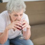 Senior woman in contemplation, drinking wine on a sofa, expressing solitude and reflection.