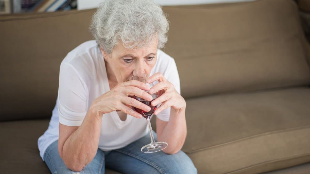 Senior woman in contemplation, drinking wine on a sofa, expressing solitude and reflection.
