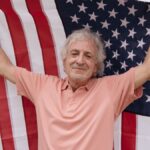Senior man joyfully holds an American flag, celebrating patriotism and independence.
