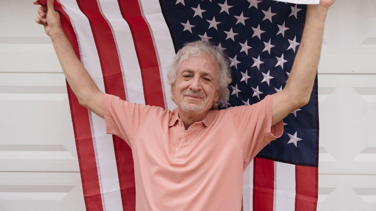 Senior man joyfully holds an American flag, celebrating patriotism and independence.