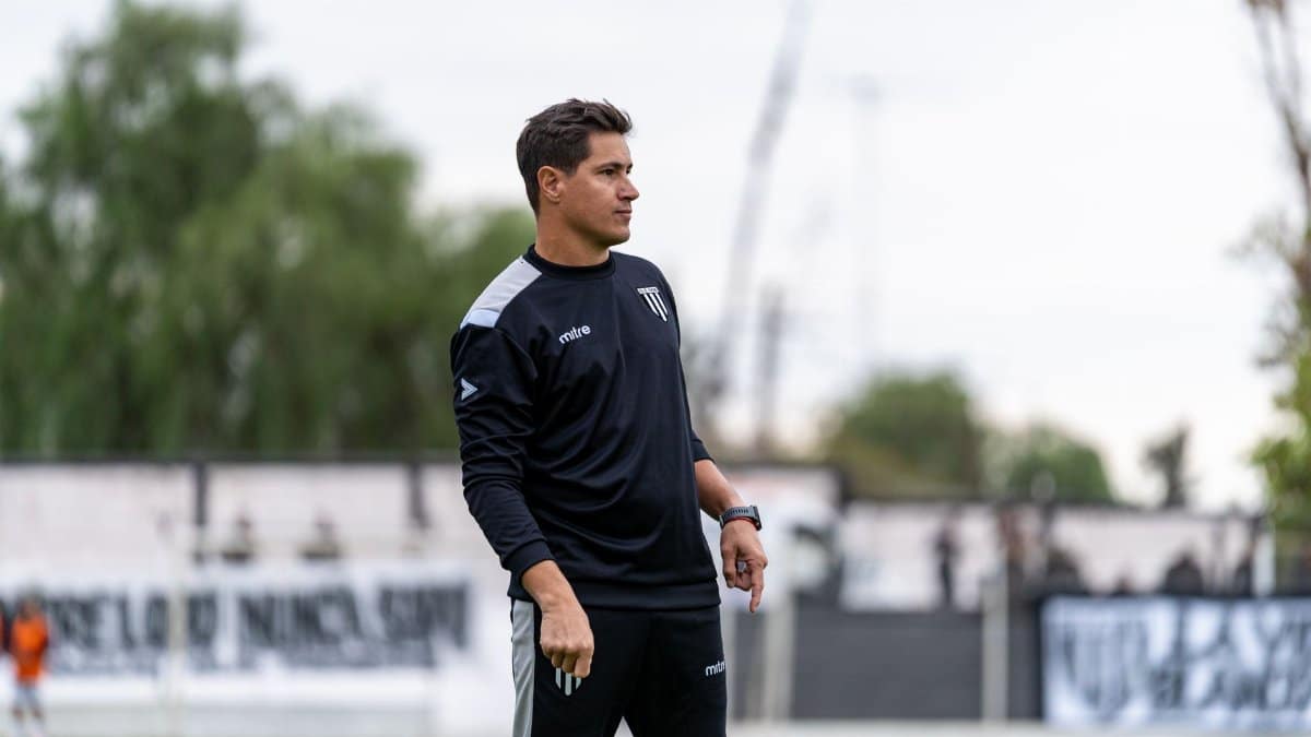 A focused football coach observes the team during outdoor practice.