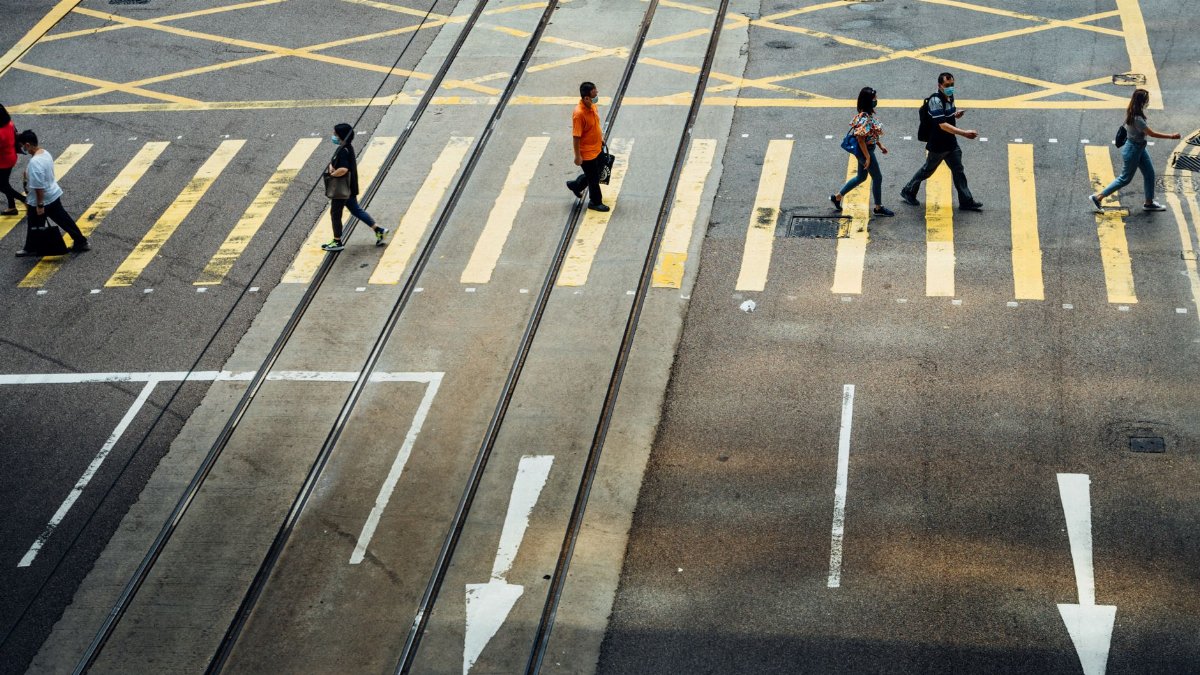 High-angle view of pedestrians crossing a street marked with bold yellow lines.