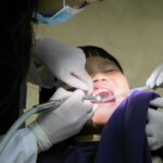 A young child receiving dental treatment from a masked dentist using dental tools indoors.