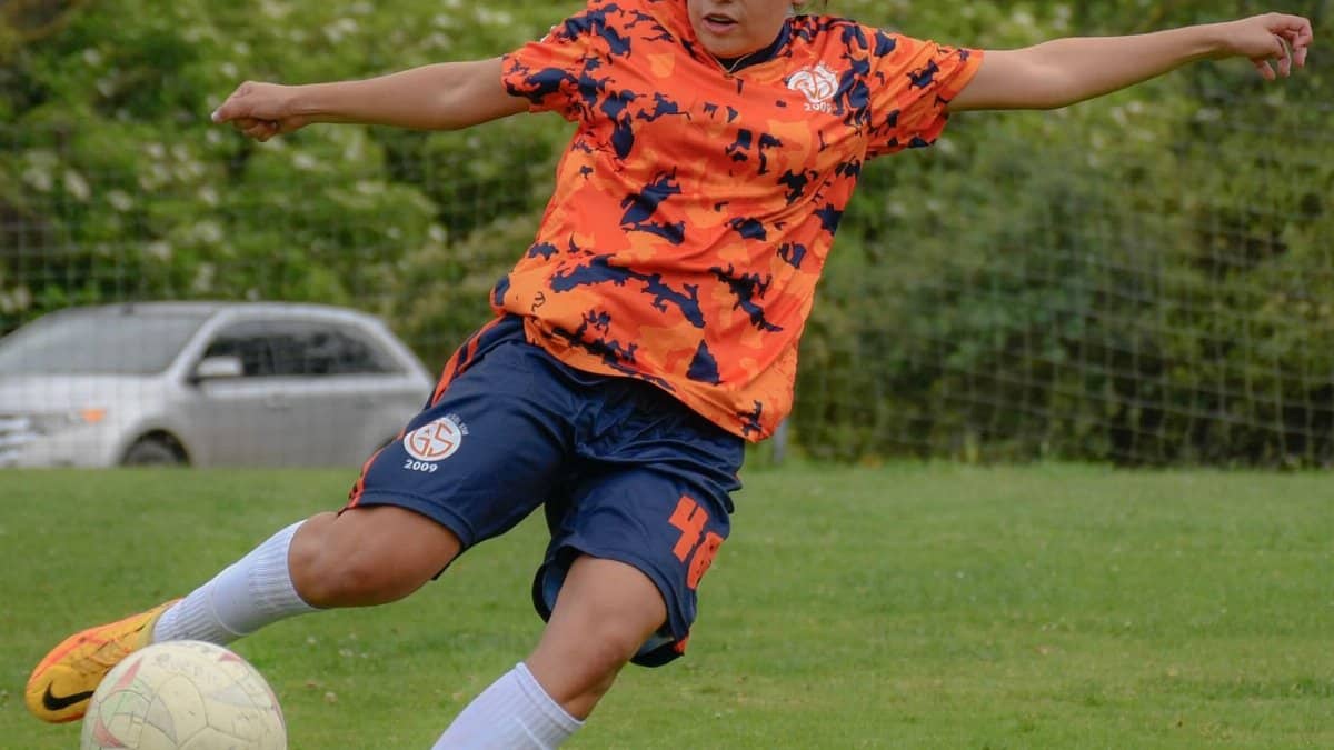 Dynamic action shot of a young female soccer player kicking the ball on a field.