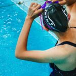 A female swimmer in a black swimsuit adjusts her cap by the pool's edge in Ciudad de México.