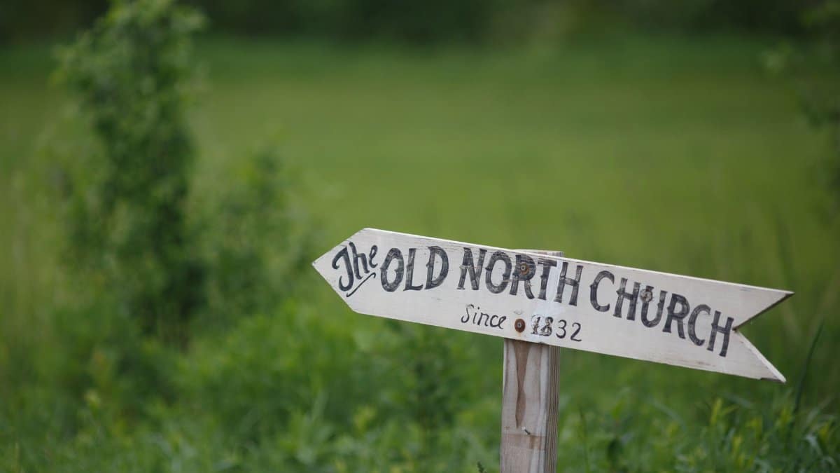 Wooden directional sign pointing to The Old North Church since 1832 in lush countryside.