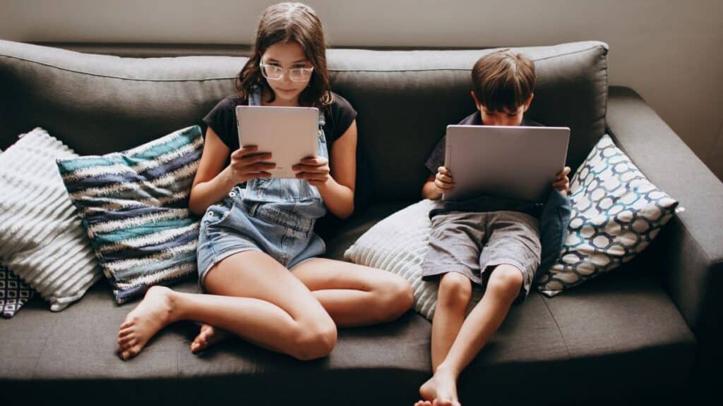 Two children engaging with tablets on a sofa, creating a modern lifestyle scene.