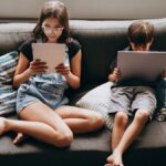 Two children engaging with tablets on a sofa, creating a modern lifestyle scene.