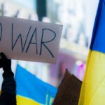 Close-up of protesters with 'No War' sign and Ukrainian flag in Times Square, New York City.