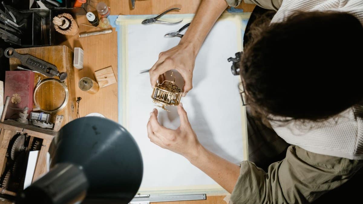 A clockmaker skillfully repairs a watch mechanism at a workshop desk surrounded by tools.