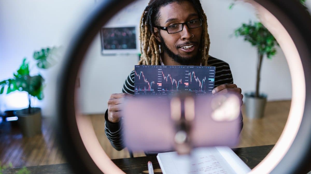 A vlogger reviews cryptocurrency stock charts in a modern setting with a ring light.