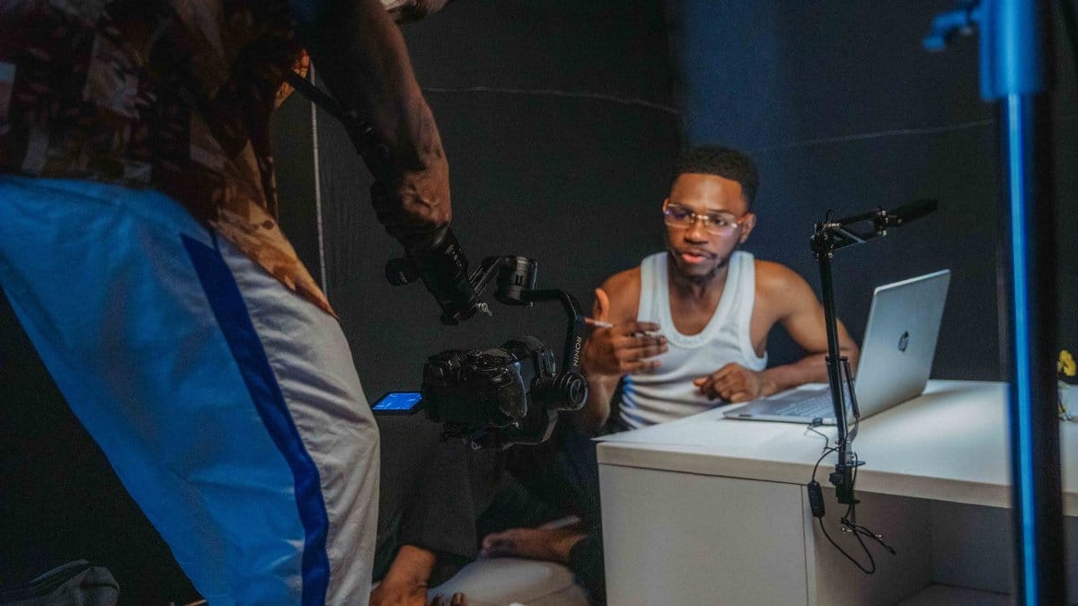 Young black men filming a casual video with laptop and camera in a home studio setting.