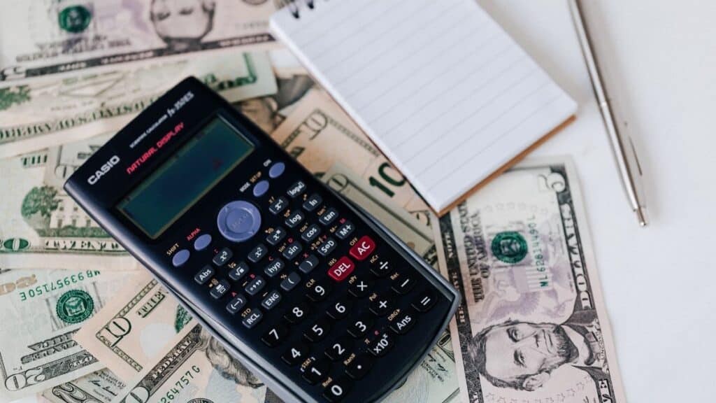 From above electronic calculator and notepad placed over United States dollar bills together with metallic pen for budget planning and calculation