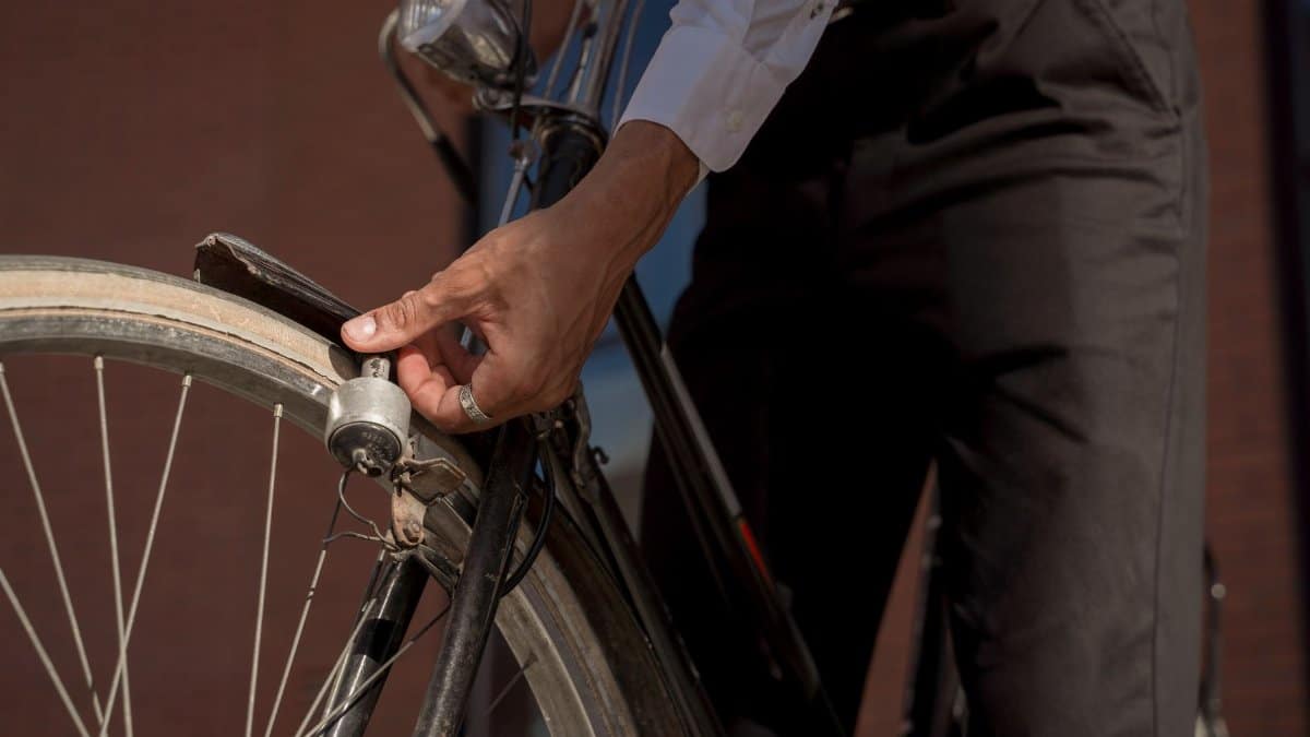 A close-up view of a person adjusting a bicycle wheel outdoors, highlighting casual attire in an urban setting.