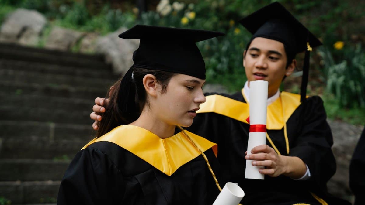 Two young graduates celebrating their achievement with diplomas and caps outdoors.