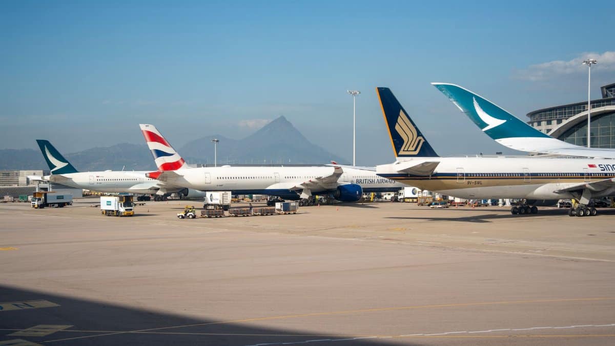 Multiple commercial airplanes parked at an airport terminal with a mountain view in the background.