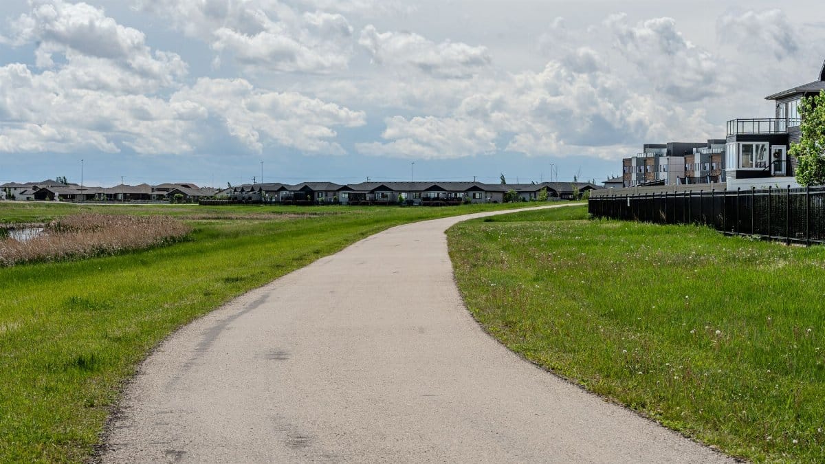 Scenic suburban pathway on a cloudy day, lined with green grass and residential buildings.