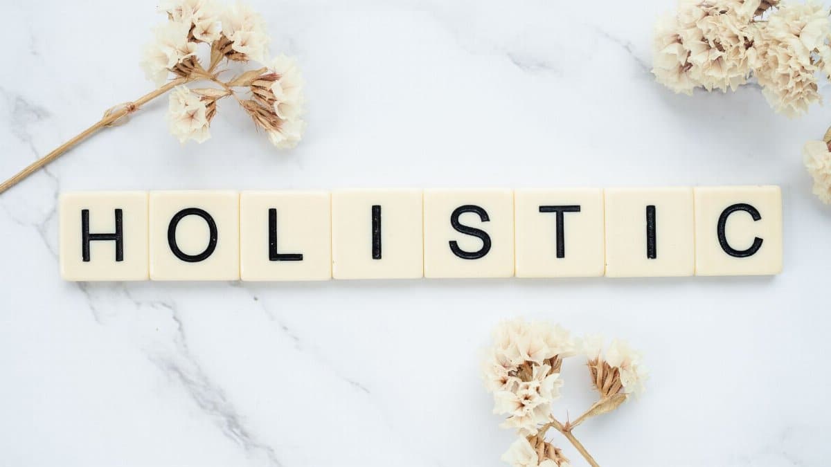 Flat lay of 'holistic' spelled in letter tiles on marble with dried flowers.
