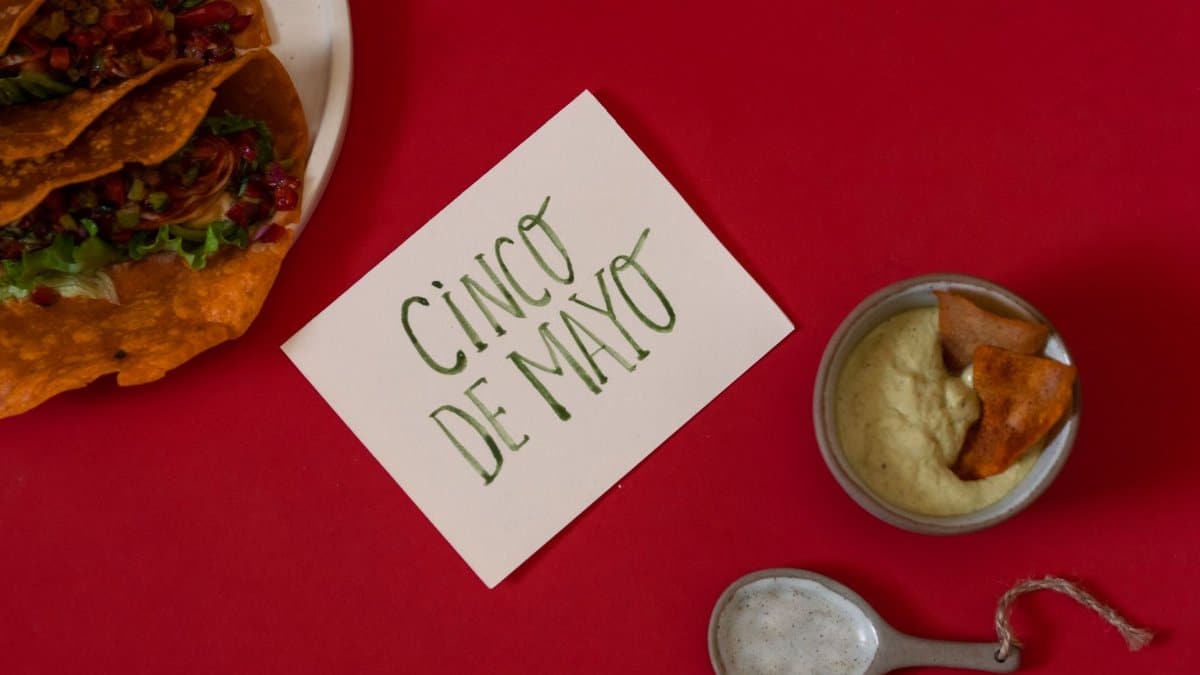 Overhead view of tacos and dip on a vibrant red background celebrating Cinco de Mayo.