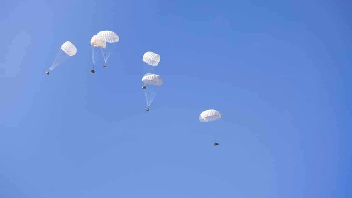 Multiple parachutes drop cargo boxes in a clear blue sky, showcasing aerial delivery technology.