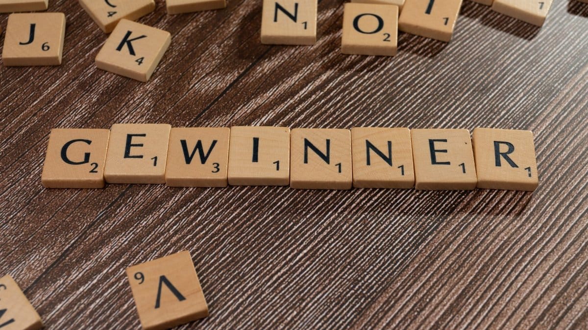 Scrabble tiles forming the word 'Gewinner' meaning winner on a wooden table.