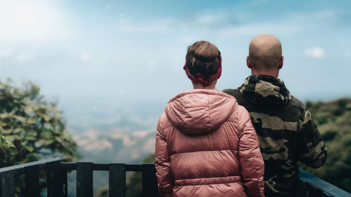 Couple in jackets standing on deck, admiring scenic mountain view.