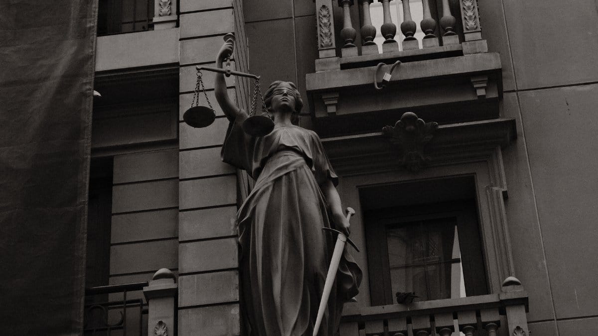 A black and white image of Lady Justice statue against a building facade symbolizing law and fairness.