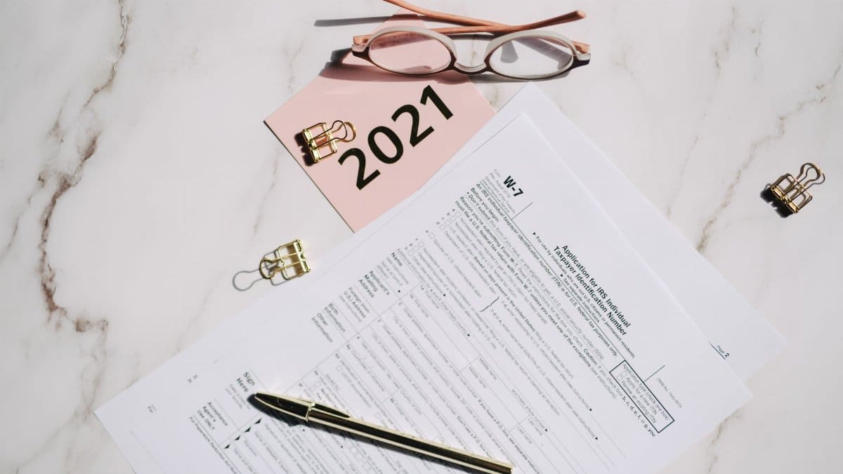 Close-up of W-7 tax forms with glasses and pen on a marble desk, ideal for finance concepts.