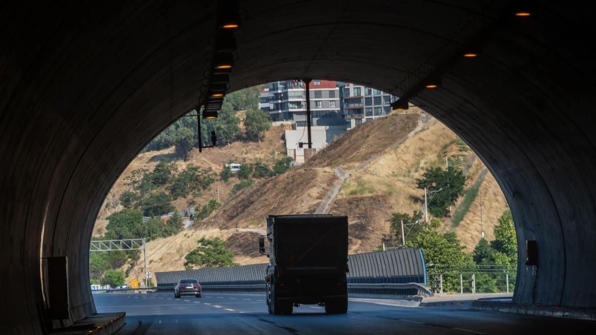 A truck exits a tunnel in İzmir, Türkiye, showcasing city and hillside view.
