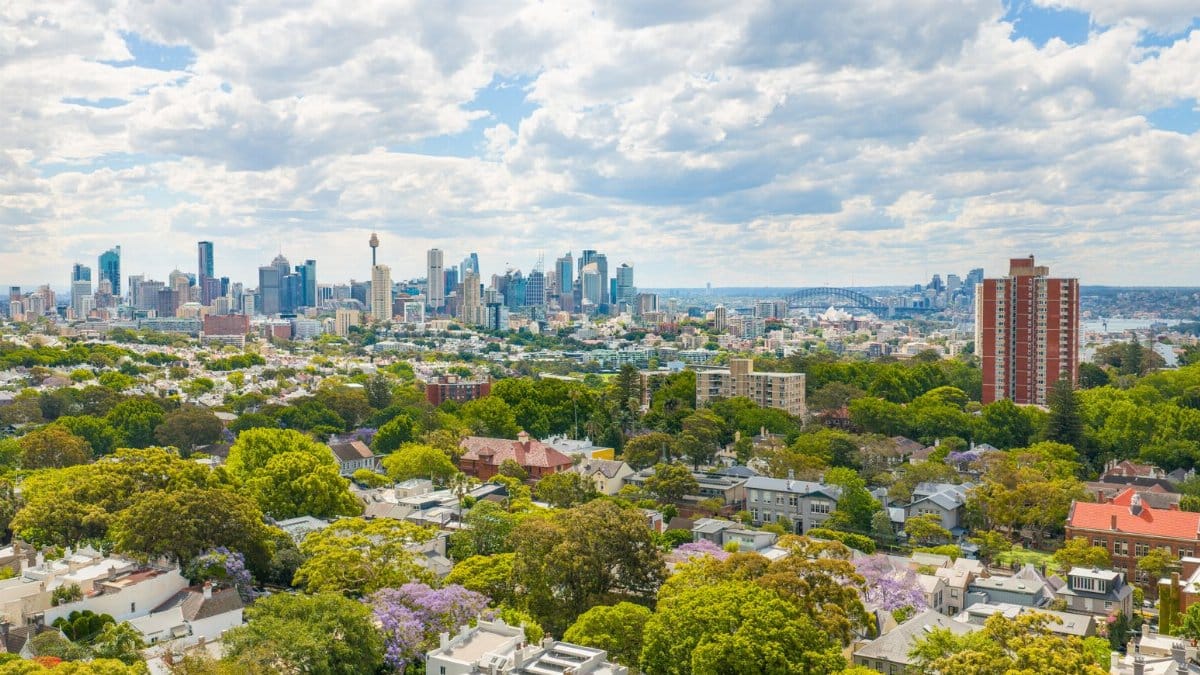 A stunning aerial view of Sydney's skyline with lush greenery in the suburbs, featuring iconic landmarks and vibrant city life.