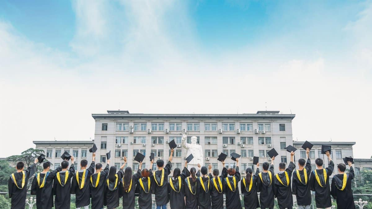 Group of graduates in gowns celebrating outdoors with a building backdrop.