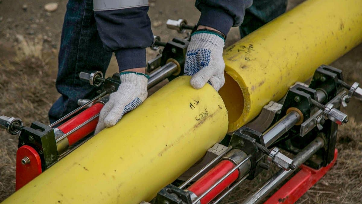 Close-up view of a worker using equipment to install yellow pipes outdoors, focusing on hands and tools.