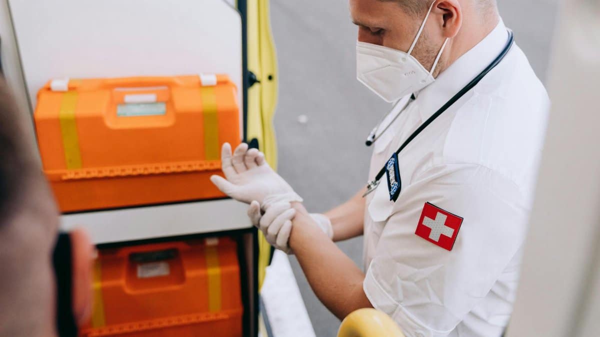 A paramedic putting on gloves next to emergency equipment inside an ambulance.