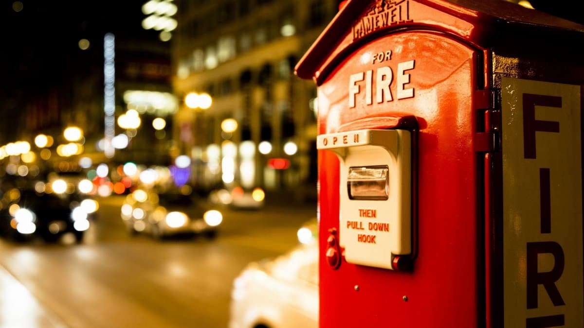 A classic red fire alarm box on a city street lit by car headlights at night.