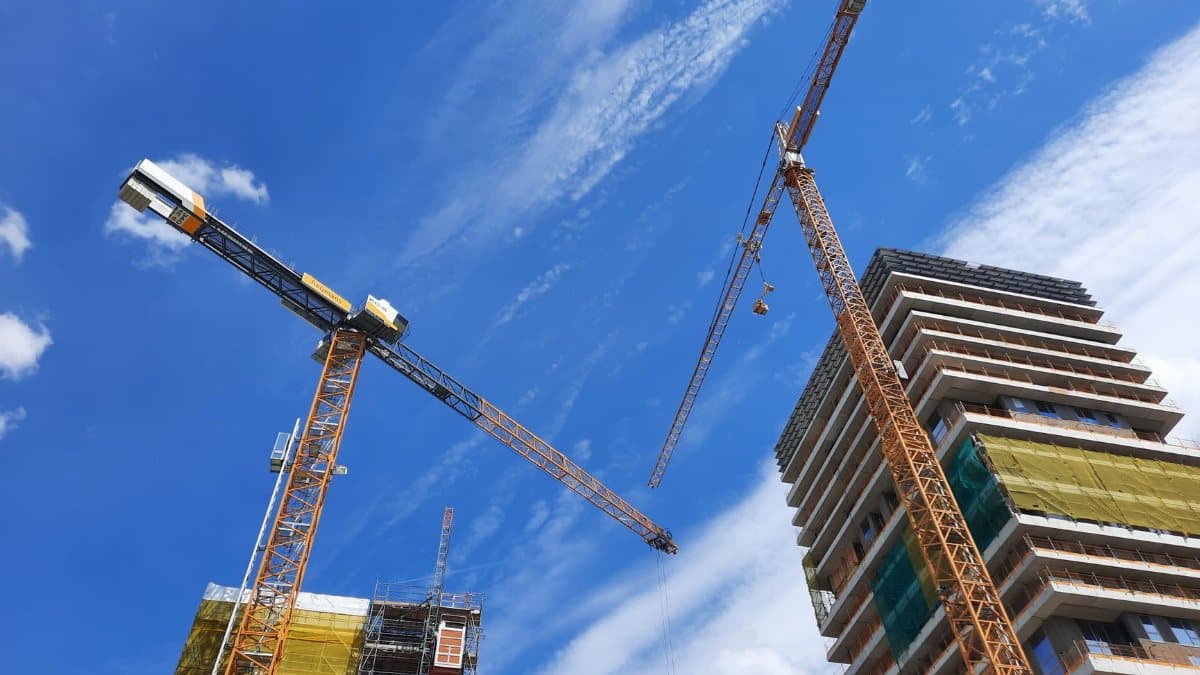 Low angle view of tower cranes and building under construction against a blue sky.